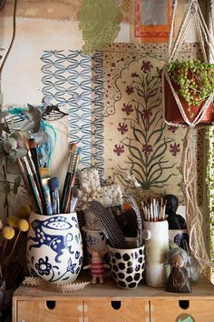 a wooden table topped with lots of vases filled with plants and art supplies in front of a wall