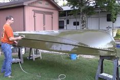 a man standing next to a green plane on top of a lush green field in front of a building