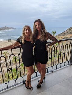 two beautiful women standing next to each other in front of a balcony overlooking the ocean