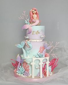 a three tiered cake decorated with pink, blue and white frosting mermaids