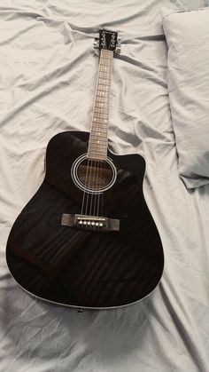 a black acoustic guitar laying on a white sheet