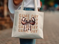 Show your team spirit with this Game Day Tote Bag featuring a unique bow football design! Perfect for sports enthusiasts, this tote bag is a great accessory for any game day outing. Whether you're heading to a football game, tailgate, or just running errands, this tote is a stylish way to show off your love for the game. It's also a perfect gift for the football lover in your life. Made with high-quality materials, this tote bag is both durable and fashionable. Make every game day special with this one-of-a-kind tote bag! Product Features: Fabric: 100% Cotton Handles: Sheeting self-fabric handles Size: 15"x16" Inches Printing: (DTG) Direct-to-Garment printing White Sporty Bag As Gift, Sporty White Bag As Gift, Sporty White Bag Suitable For Gifts, White Letter Print Sports Bag, Spirit Bags, Unique Bows, Football Lover, Football Lovers, Football Design