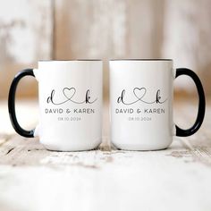 two black and white coffee mugs sitting on top of a wooden table next to each other