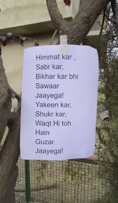 a sign hanging from a tree in front of a building that says himmat kar, sabar kar, bhakar kar,