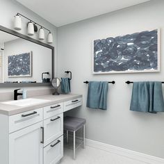 a white bathroom with blue towels hanging on the wall and two mirrors over the sink