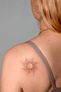 the back of a woman's shoulder with a small sun tattoo on her upper arm