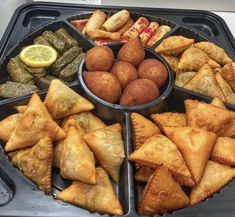 a tray filled with different types of pastries and pickle slices next to lemon wedges