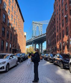 a woman is standing on the sidewalk in front of some parked cars and a bridge