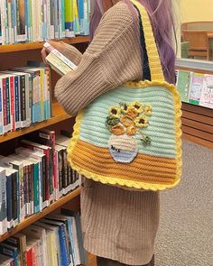 a woman holding a crocheted bag in front of a book shelf filled with books