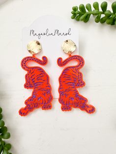 "GO TIGERS! These acrylic tiger earrings are the perfect accessory for game days and to show off your team spirit! This listing is for one pair of orange acrylic tiger earrings and are completed with gold circle studs! Choose between black, navy or purple tiger stripes. *These stripes are hand painted onto the acrylic. If you want a different color combination, please don't hesitate to send us a message! Acrylic Hand Painted Tigers Approximate size:  3.25\" L x 1.5\" W These are only available in limited quantities. Due to the handmade nature of this item, pattern placement may vary. Are you new to cork, leather and acrylic earrings? They are lightweight, the perfect accessory to ANY outfit and highly addicting! Love this earring style but need different school/team colors or a bigger size Bengals Clay Earrings, Orange Statement Earrings, Tiger Clay Art, Tiger Earrings Clay, Clemson Earrings, Tiger Tree Earrings, Tiger Earrings, Tiger Stripes, Purple Earrings