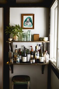 a shelf filled with bottles and glasses on top of a wall next to a window