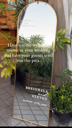 a large mirror sitting on the side of a sidewalk next to potted plants and trees