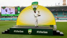 a man holding a trophy standing on top of a green and black platform in front of a stadium