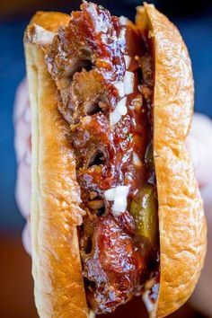 a hand holding a sandwich with meat and vegetables