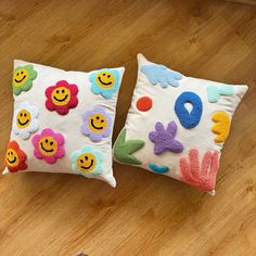 two decorative pillows sitting on top of a wooden floor next to each other with smiley faces painted on them