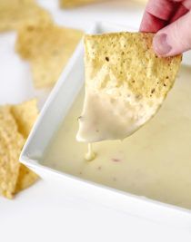 a hand holding a tortilla chip over a bowl of dip