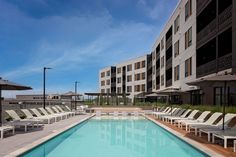 an empty swimming pool with lounge chairs and umbrellas in front of the hotel building