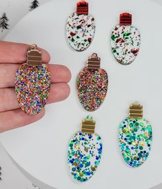 a hand holding four different colored and glittered christmas ornament ornaments on a white table