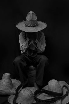 a man sitting on top of a pile of straw hat's and other hats