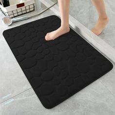 a person standing on a bathroom floor next to a black mat with circles and dots