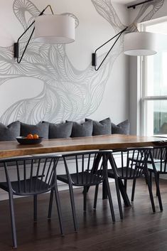 a dining room table and chairs in front of a wall with an artistic design on it