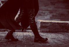 a woman walking down the street with an umbrella over her head and black boots on