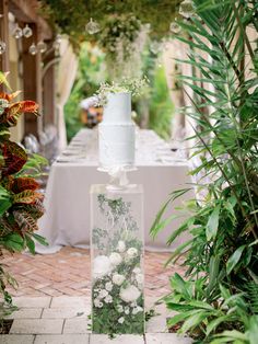 a white wedding cake sitting on top of a table covered in flowers and greenery