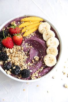 a bowl filled with fruit and granola on top of a white countertop next to a spoon