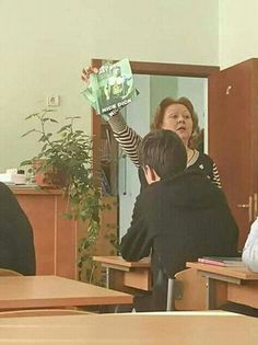 a group of people sitting at desks with one person holding up a book in the air