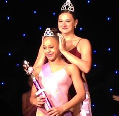 two women standing next to each other in front of blue lights and one holding a trophy