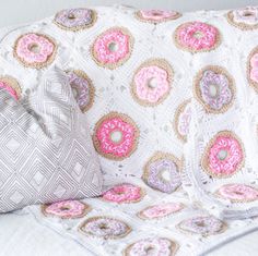 a white crocheted blanket with pink and blue donuts on it next to a pillow