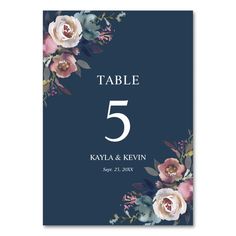 a table number card with flowers and leaves on the front, in navy blue background