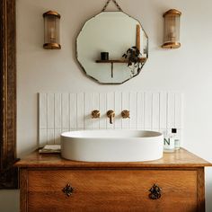 a white sink sitting on top of a wooden dresser next to a wall mounted mirror