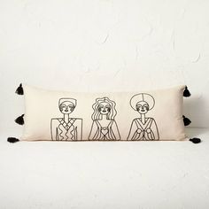 a pillow with three people drawn on it and black tassels around the edges