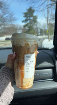 a woman holding up a cup of iced coffee in her hand while sitting in the passenger seat of a car