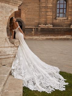 a beautiful woman in a wedding dress leaning against a stone wall with her back to the camera