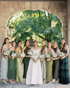 a group of women standing next to each other in front of a stone arch holding bouquets