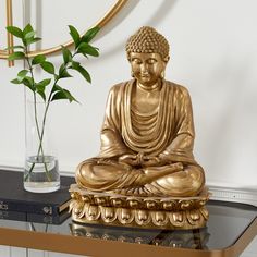 a golden buddha statue sitting on top of a table next to a vase with a plant