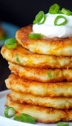 a stack of pancakes topped with sour cream and green onions on a white plate sitting on a wooden table