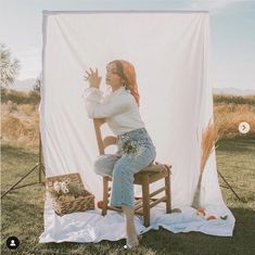 a woman sitting on top of a wooden chair in front of a white sheet covered backdrop