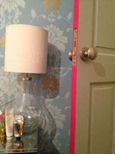 a lamp on a table in front of a blue and pink wallpapered room