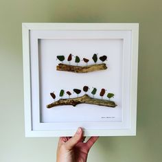 a person holding up a framed art piece with birds on branches in the shape of trees