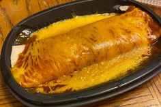 an enchilada in a black dish on a wooden table