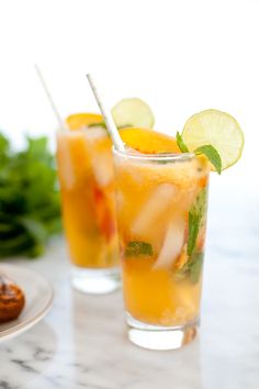 two glasses filled with drinks and garnished with limes on a marble table