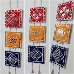 four different colored tiles hanging from hooks on a wall with bells attached to the sides