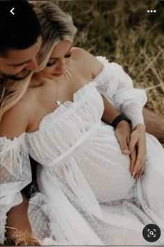 a man and woman sitting next to each other on the ground in front of grass