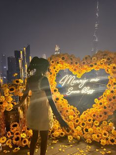 a woman standing in front of a heart - shaped display with sunflowers on it