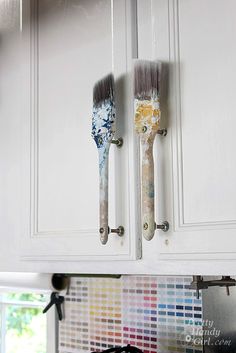 two paintbrushes are stuck to the wall in front of white cabinets with colorful tile backsplash