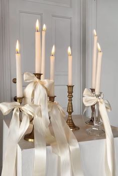 a table topped with candles covered in white satin ribbons and bowknots on top of it