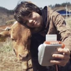 a young boy is petting a baby cow in the field while holding an electronic device